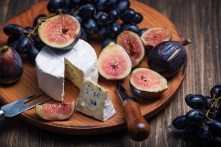 Cuted blue cheese, fresh fig halfs and grapes on rustic wooden plate. Moody scene with selective focus.の写真素材