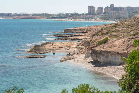 Orihuela Costa, Spain - June 16, 2018: People sunbathing and swiming at the Cala Capitan beach in the Cabo Roig, popular place for holidaymakers. Province of Alicante. Costa Blanca. Spain.の写真素材