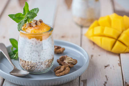 Homemade pudding of Chia seeds and almond milk with cereals and puree of mango and kiwi with walnuts and mint in glass jars. Vegan healthy morning breakfast or superfood dessert on the rustic wooden table.の写真素材