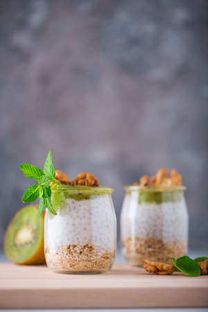 Homemade pudding of Chia seeds and almond milk with cereals and puree of kiwi with walnuts and mint in glass jars. Vegan healthy morning breakfast or superfood dessert on the wooden table.の写真素材