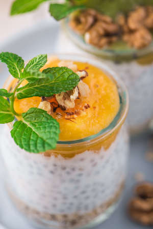 Top view of Homemade pudding of Chia seeds and almond milk with cereals and puree of mango and kiwi with walnuts and mint in glass jars. Vegan healthy morning breakfast or superfood dessert on white dish.の写真素材