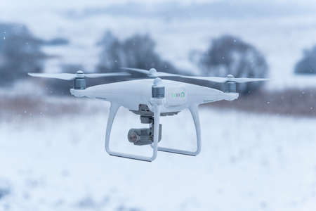 Hovering drone taking pictures of wild nature. Cold winter weather. Cloudy day with falling snow.の写真素材