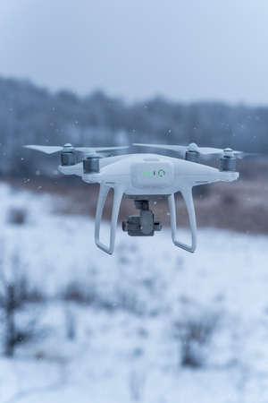Hovering drone taking pictures of wild nature. Cold winter weather. Cloudy day with falling snow.の写真素材