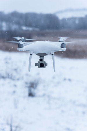 Hovering drone taking pictures of wild nature. Cold winter weather. Cloudy day with falling snow.