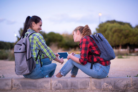 two young women students with backpack holding and looking at the tablet and smiling. Girl shows something on the screen.の写真素材