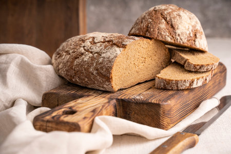Sliced loaf of black bread on the old rustic wooden cutting board. Selective soft focus