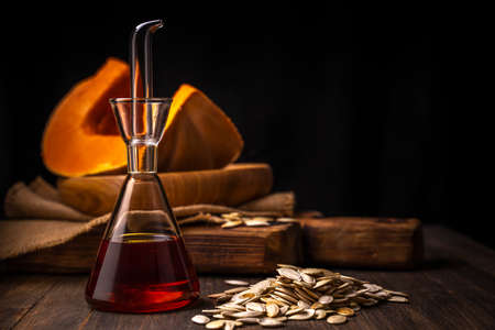 Fresh organic pumpkin seed`s oil in the glass bottle on rustic wooden background close up selective focus.の写真素材
