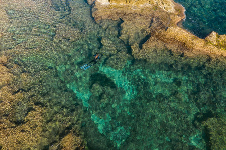 Aerial drone bird's eye view of swimming spearfishing diver in rocky seascape located in Costa Blanca, Torrevieja, Spain.の写真素材