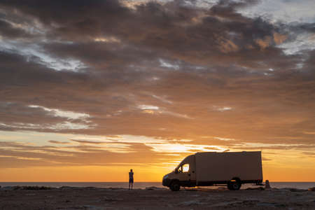 sunset / sunrise at rocky seaside with travel trailer. Dramatic and calm cloudy sky with sun beams.の写真素材