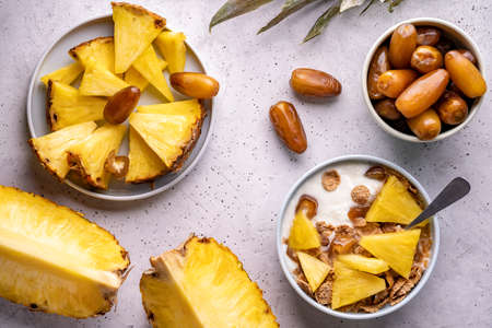 Healthy breakfast bowl: dates with fresh pineapple, homemade granola, corn flakes on light gray background. Flat lay selective focusの写真素材