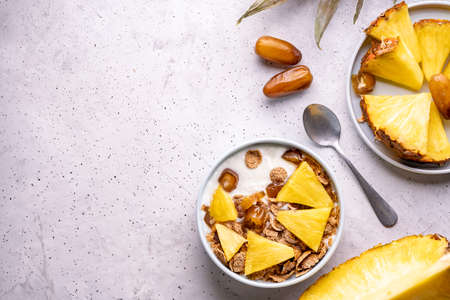 Healthy breakfast bowl: dates with fresh pineapple, homemade granola, corn flakes on light gray background. Flat lay selective focusの写真素材