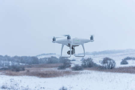 Hovering drone taking pictures of wild nature. Cold winter weather. Cloudy day with falling snow.の写真素材
