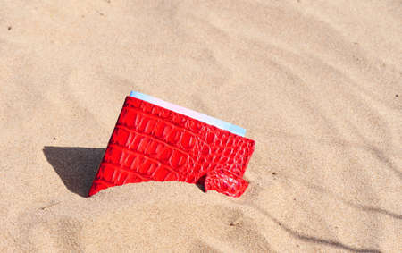 Textured sand background on the river Bank, a red purse with a piece of banknote looks out of the sand. Backgrounds and textures.の写真素材