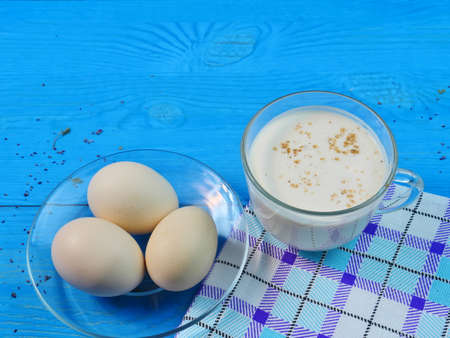 Village eggs in a plate, a Cup of milk on a napkin, on a blue background. Close-up, Correct...