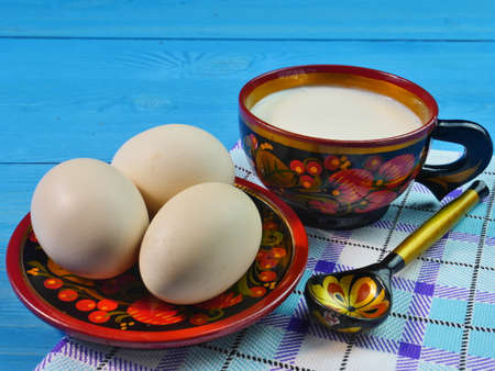 Khokhloma-chicken eggs in a Cup on a blue wooden background. A Cup of Khokhloma with milk. Close up. Dietary food.の写真素材