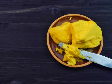 A clay plate with rustic butter and a knife on a black wooden background. Close up.