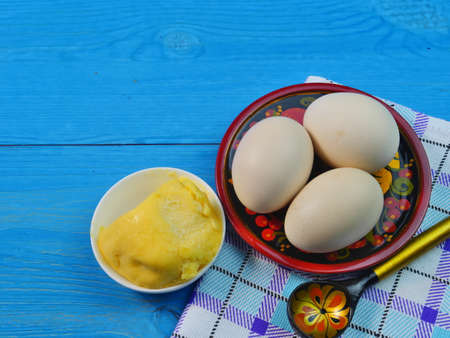 Rustic chicken eggs in a Cup on a blue wooden background. A Cup of butter. Close up. Dietary food.の写真素材