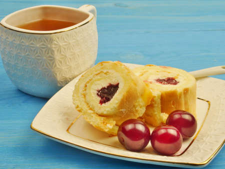 A cup of tea and cream rolls in a bowl with cherries on a gogle-lingyed background.の写真素材