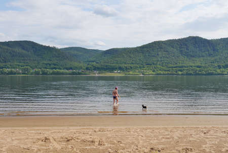 A young woman on the sandy beach of the Volga river bathing with a dog. Sports and recreation. Lifestyle.の写真素材