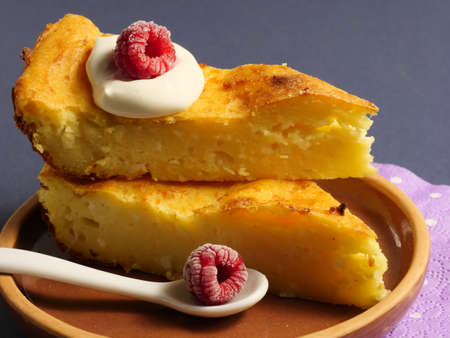 Cottage cheese casserole with raspberries and sour cream on a white platter. Close up. Good...