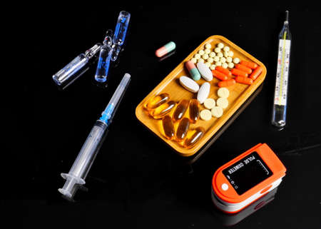 Pulse oximeter, syringe, pills, thermometer, on a plate, on a black background, Close-up,の写真素材