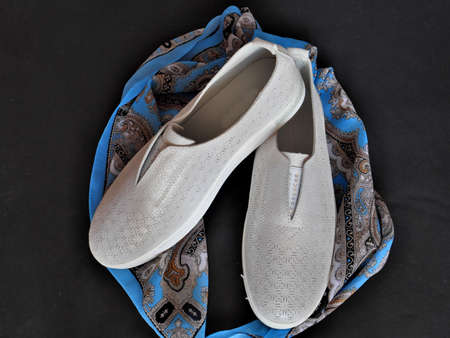A pair of white women's shoes and a blue scarf on a black background.