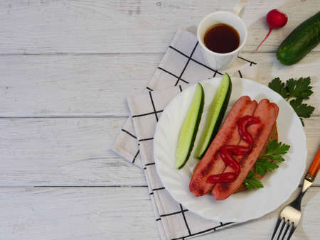 Sliced hot dog on a white plate with cucumber, radish and parsley.の写真素材