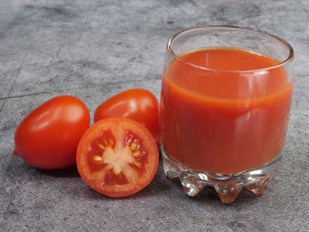 Tomato juice in a glass and ripe tomatoes on a gray backgroundの写真素材
