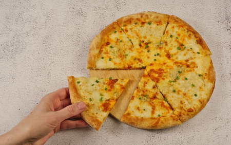Pizza with cheese and herbs in hand on a light background.