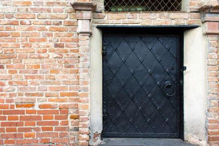 Black iron door with riveted stripes in an old red brick wall.の写真素材