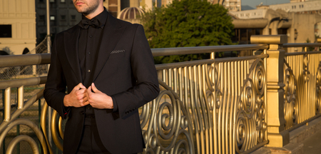 Male model in a black suit posing next to a golden fenceの写真素材