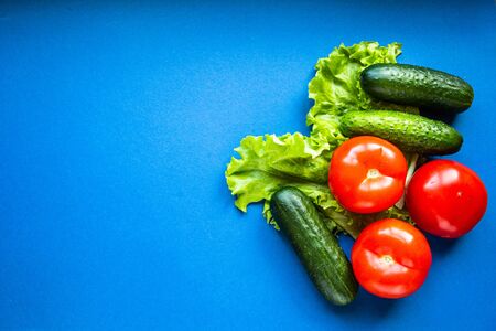 Fresh vegetables on a blue dackground. Cucumbers, tomatoes and lettuce. Healthy eating and vegetarianism conceptの写真素材