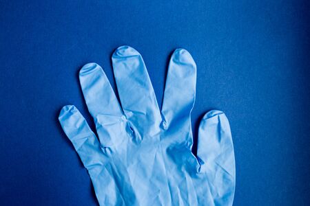Prevention from of coronavirus. Close-up medical protective glove on a blue background. Protection against danger COVID-19の写真素材