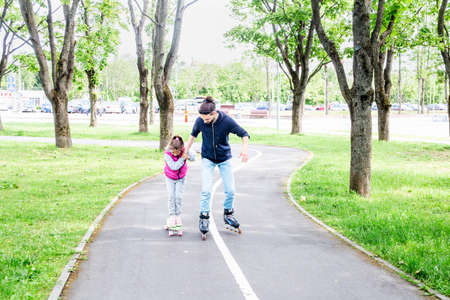 Family activities in the summer park. Happy father teaching little daughter to roller skating in...