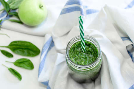 Healthy green smoothie with spinach and apple in a mug with a strip of linen cloth on a white table...