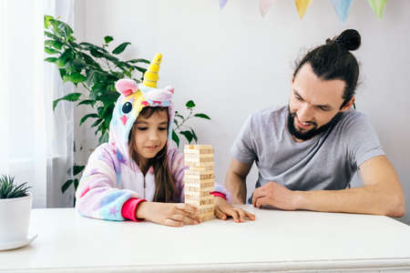 Lifestyle family activites and offline games. Cheerful bearded father with daughter plays board game at home.の写真素材