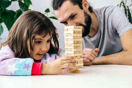 Close up cute little daughter with her young father plays board game at home. Lifestyle family spend time, home family activites and gamesの写真素材