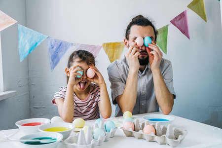 Happy family getting ready to Easter celebrate at home. Adorable little girl and her having fun while while dyed easter eggs.の写真素材
