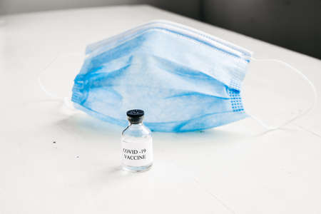 Coronavirus vaccine in a bottle with blue protective face mask on the table prepared for vaccinating. COVID19 Vaccine researching and development concept.の写真素材