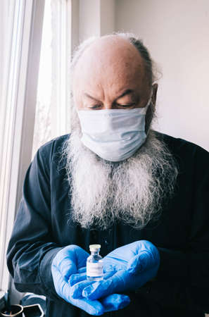 Covid-19 vaccination for the elderly. Portrait of an bearded senior man wearing a medical mask and holding an ampoule with a coronavirus vaccine.の写真素材