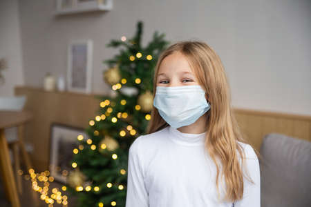 Little girl wearing protective mask on Christmas room background. Christmas festive and social distancing during   pandemic concept.の写真素材