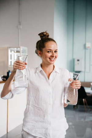 Attractive young woman in white casual outfit holding two glass reusable bottles with clear water. Healthy life and water consumption rate conceptの写真素材