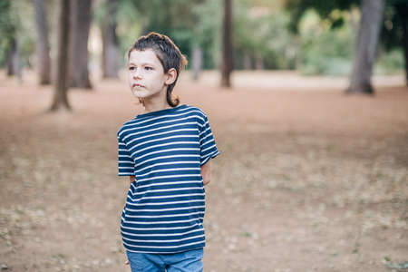 Outdoor portrait of unhappy autism schoolboy in a closed position. Autistic boy excited while walking in the park.の写真素材