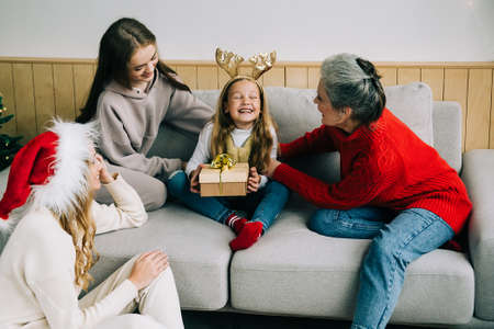 The family celebrate Christmas together. Grandmother, mom and sister give a gift to a little girl....