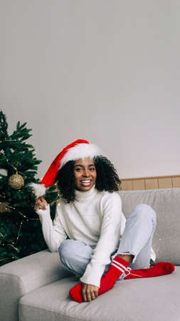 Happy Christmas Woman in Santa Hat. Smiling african american young woman Celebrating Christmas at home. Vertical photo for social media, copy space for textの写真素材