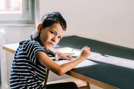 A middle school autism boysits at the table and writes in a notebook at home. Aspeger syndrome and autism invisible diseases everyday lifeの写真素材
