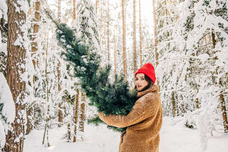 Stylish young woman picking a Christmas tree in the winter snowy forestの写真素材
