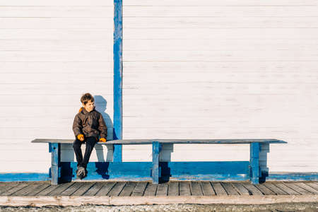 Loneliness and misunderstanding of people with autism concept. Alone autism boy sits on a blue bench against the background of a white wall.の写真素材
