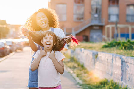 Cheerful girl have fun and fool around with her babysitter in sun lights outdoor. Girl with dyed...