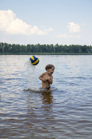 Boy with ball in water, hot summer dayの写真素材